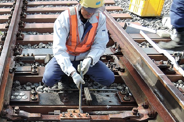鉄道のポイント部分で作業員が工具を使って保守作業をしている様子