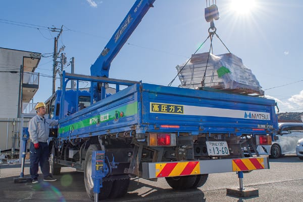  青いクレーン付きトラックで荷物を吊り上げ作業する現場風景