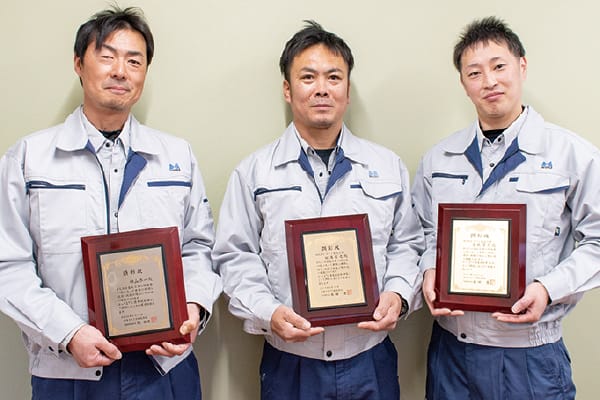 表彰状を手にした3人の作業員が笑顔で並ぶ記念撮影写真