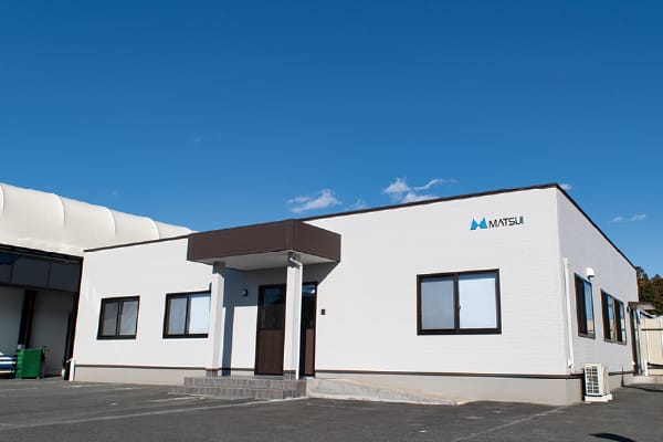 白くシンプルな建物が青空の下に立ち、「MATSUI」のロゴが外壁にある